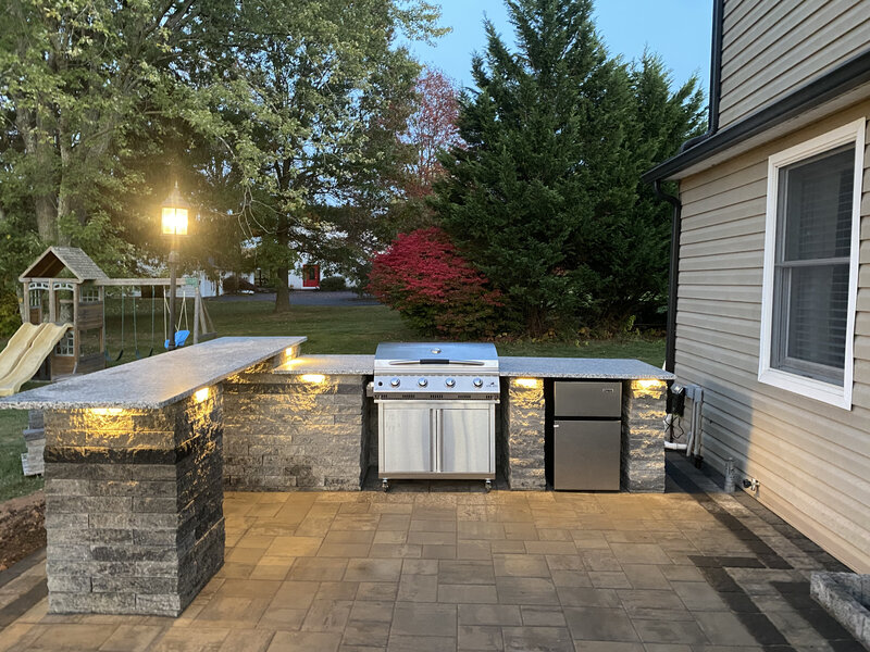 Outdoor kitchen built in on a paver patio with a kids play set in the background