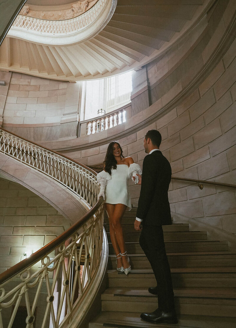 The groom extends his hand to the bride to help her descend the stairs.
