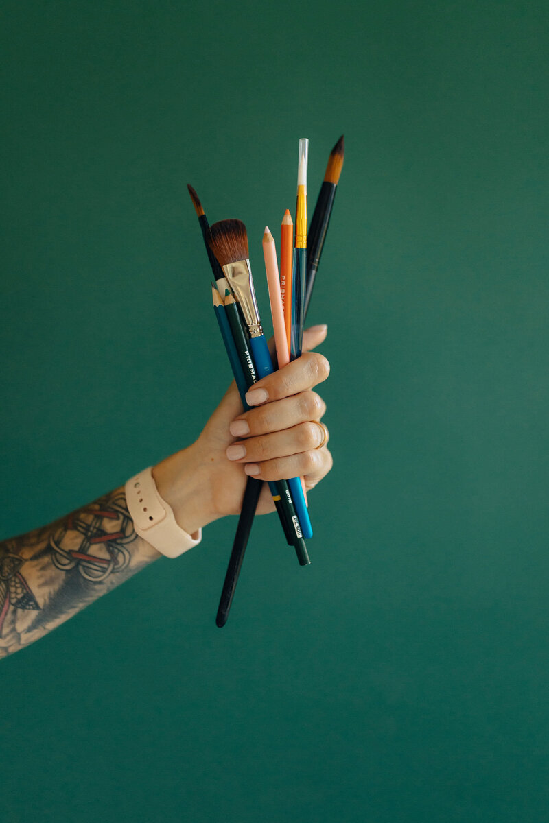 hand holding paint brushes and pencils