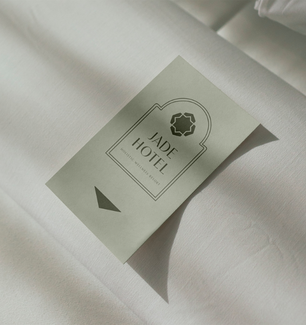 Shows a mockup of a hotel key card with a logo for Jade Hotel Holistic Wellness Resort laying on a white hotel bed