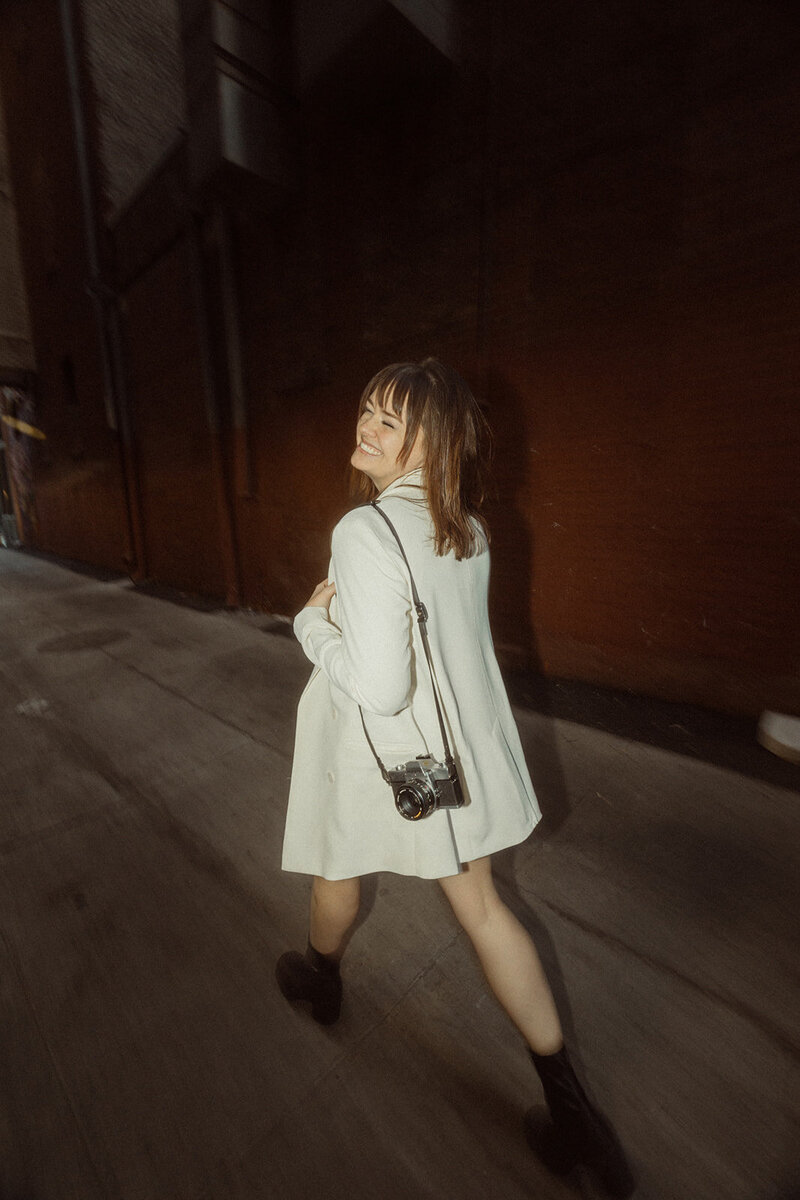 kmm photography wearing white blazer with film camera and walking away 