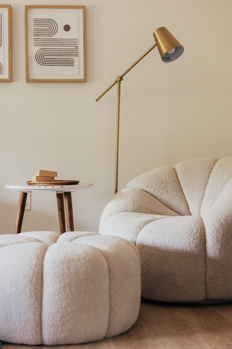 A sitting corner featuring a cushy chair, ottoman, modern gold reading lamp and a side table with books.
