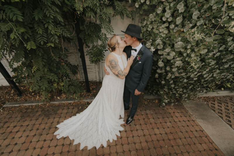 Bride and groom kissing, surrounded by greenery