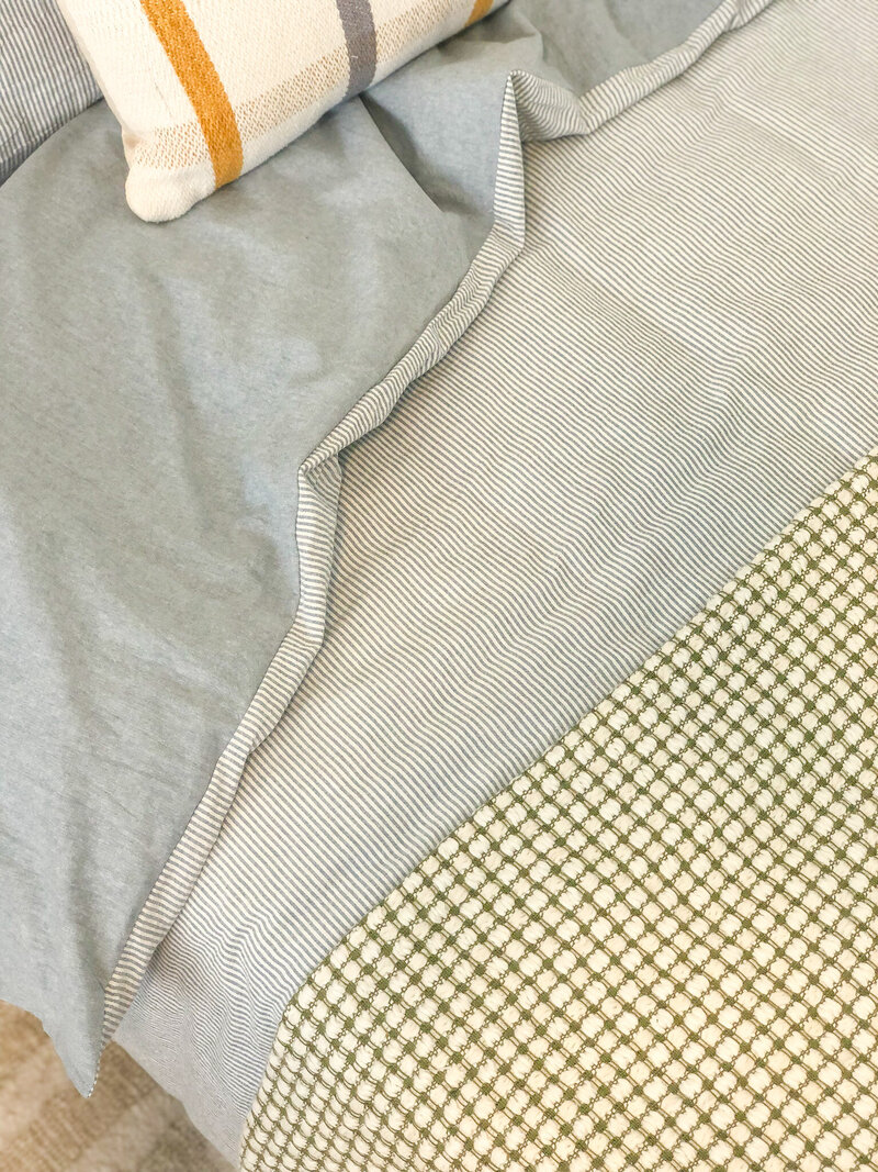 Close-up of a neatly made bed with a striped and checkered duvet, along with a pillow featuring stripes, showcasing the expert touch of Newcastle Interior Designer craftsmanship.