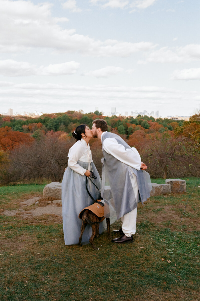 A couple shares a kiss while wearing traditional Hanboks during their fall elopement, with their dog by their side — captured on film by a film wedding photographer at Castillo Holliday Photo + Film.