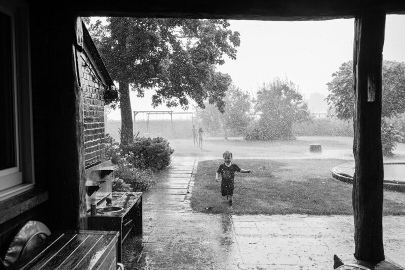 gezinsfoto buiten in de tuin. Kinderen rennen lachend in de regen. Stampen in plassen.
