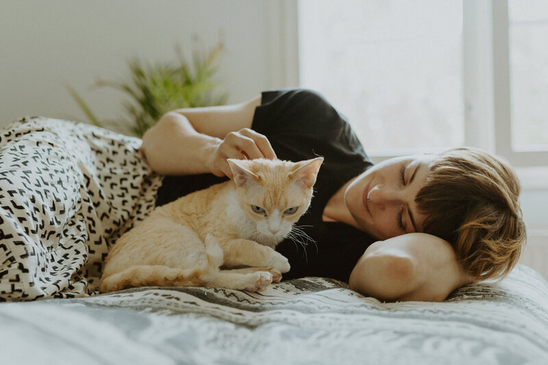 Muotokuva naisesta, joka makoilee sängyllä ja silittää kissaa