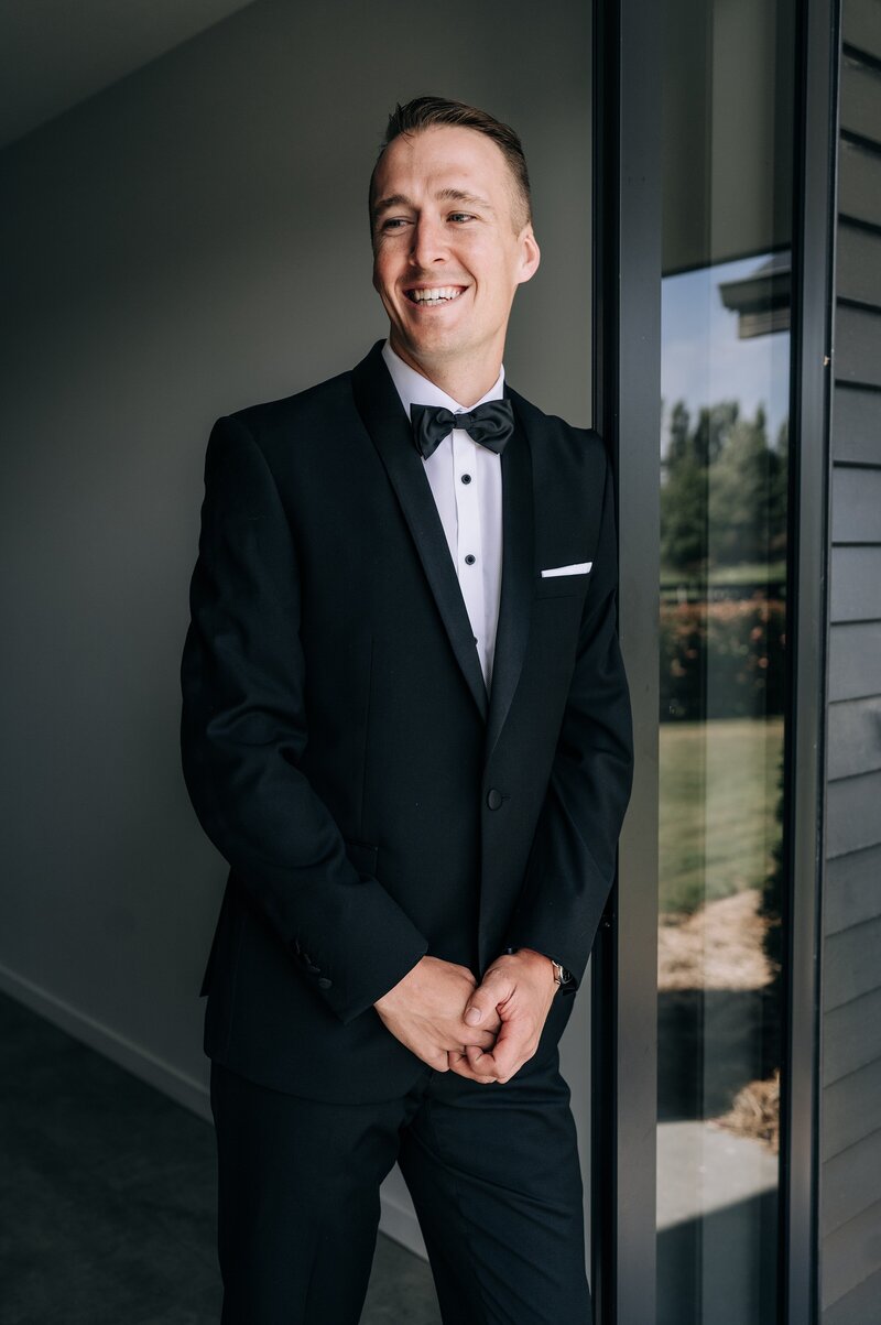 groom in a tuxedo leaning against door frame before his wedding