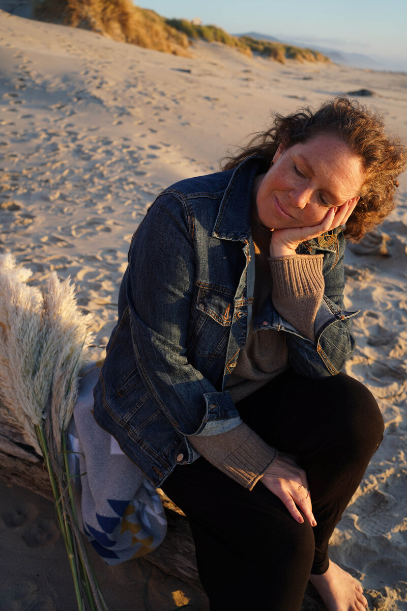 Smiling woman resting her face on her hand while sitting on a beach log