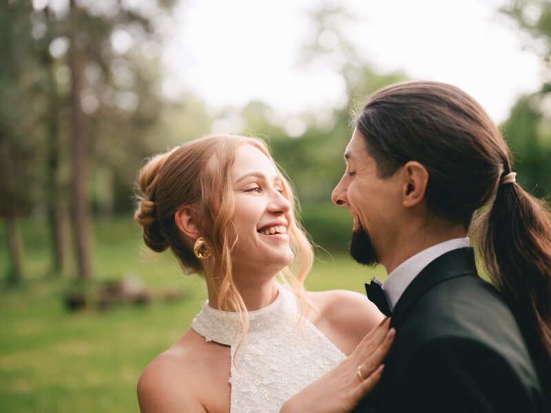 A joyful couple shares a romantic moment outdoors in a green park setting during their wedding celebration.