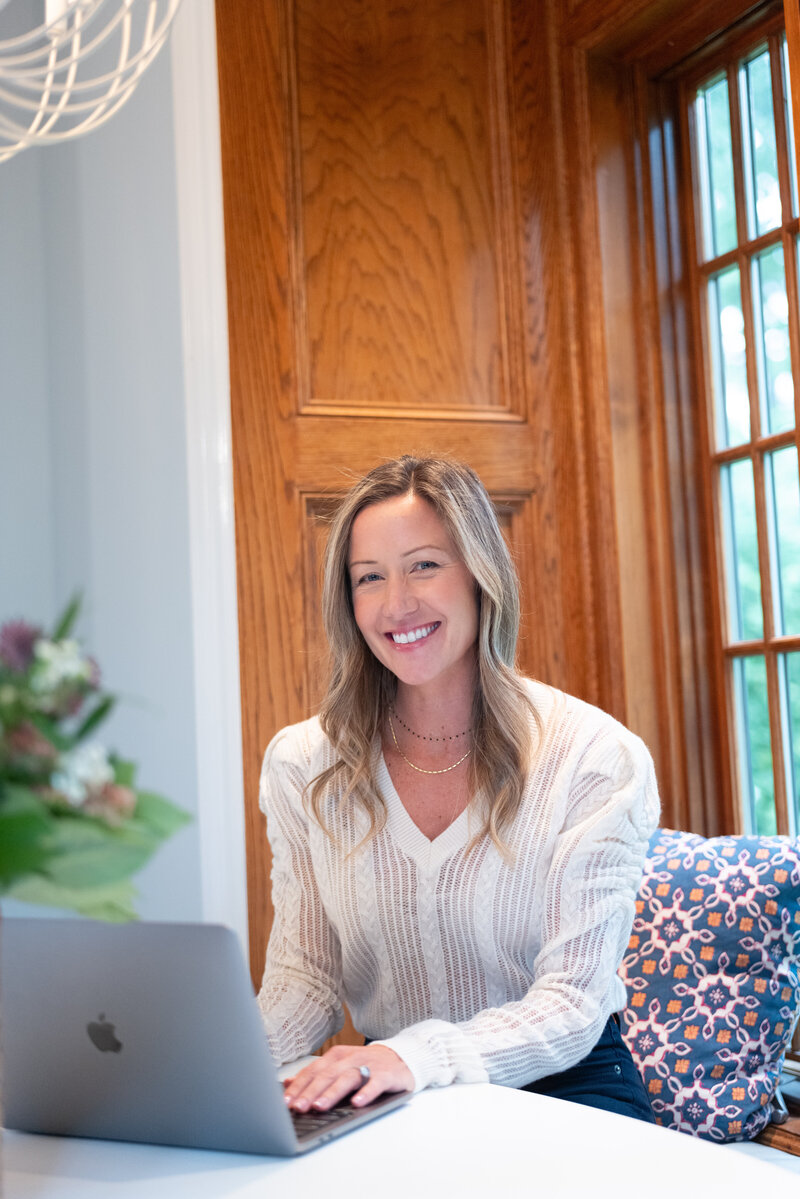 Jen, an integrative health coach, working at her computer and smiling, reflecting her positive and enthusiastic approach to her work and client interactions.