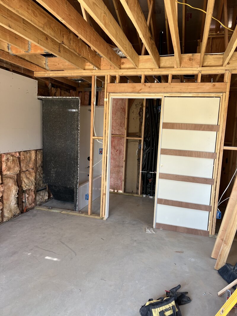 A room in the middle of remodeling with exposed ceiling rafters and no flooring.