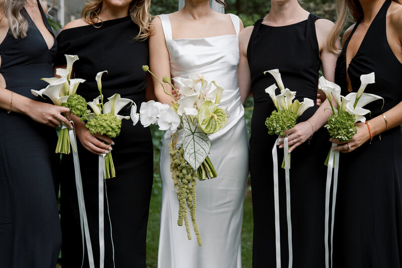 Bridesmaids in elegant black dresses holding sculptural white bouquets.