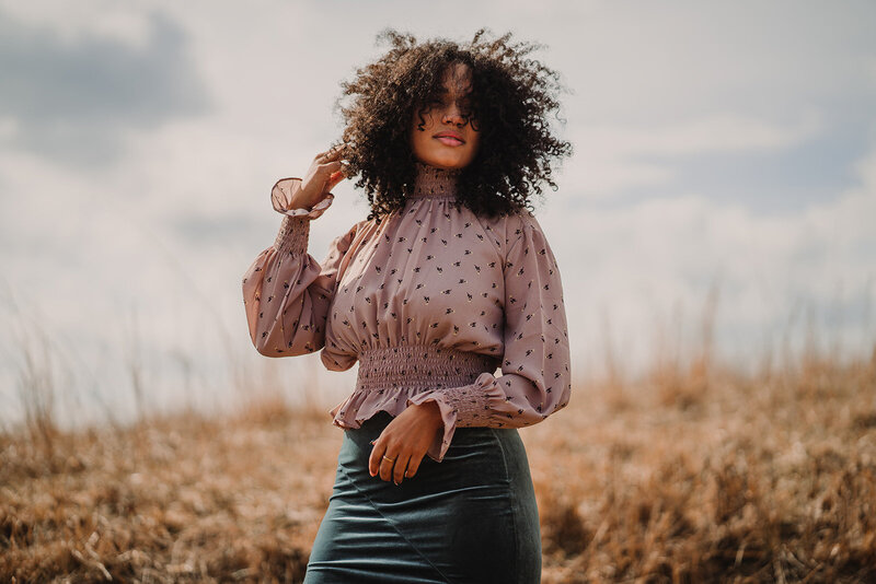 Woman with natural hair poses in the wind in a field in Tennessee in thrifted clothes.