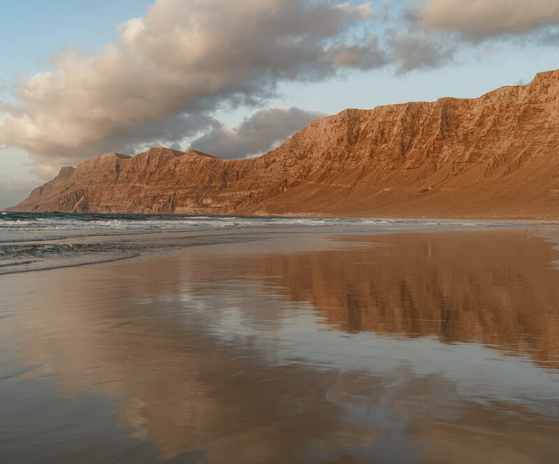 Paysage volcanique sur une plage de Lanzarote, entre sable noir et lumière dorée – décor naturel typique des Canaries