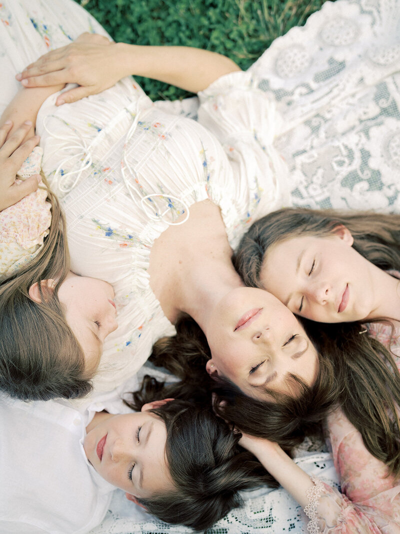 A mother lays on the ground head-to-head with her three children.