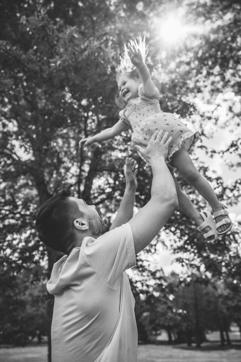Dad throwing daughter in the air and her arms are wide open and she's smiling genuinely. 