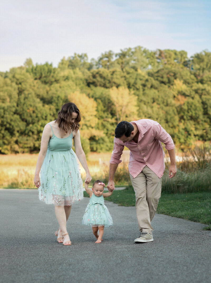 mom and dad walking in park with daughter for family photos