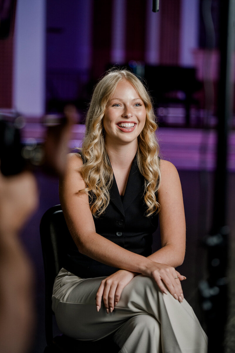 a woman smiles broadly sitting under a boom microphone while she is interviewed