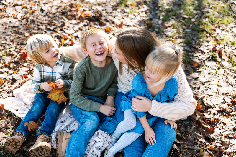 Mother sitting with her three children on a blanket and leaves during a fall session in Farmington, Missouri. 