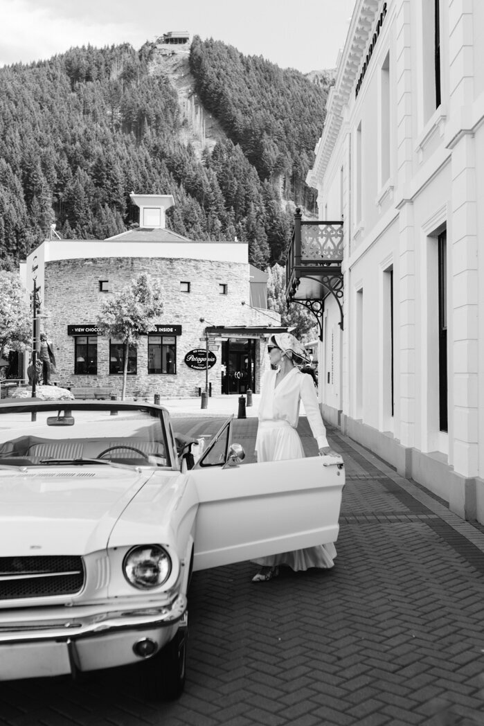 The Lovers Elopement Co - black and white photo of classic car outside Eicharts on the lake front of Queenstown with female opening door