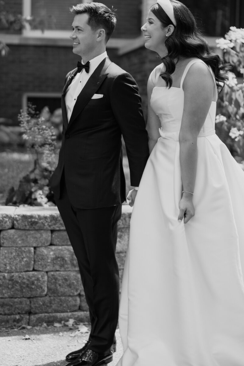 Black and white image of brunette bride and groom smiling while talking to someone