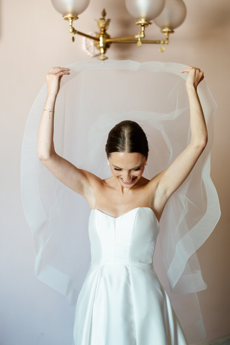 Bride smiling and lifting veil in soft natural light, strapless wedding gown, elegant bridal portrait | Ohio wedding photographer
