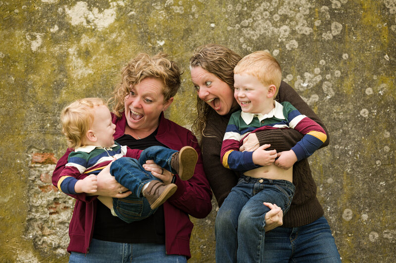 A same-sex couple snuggling their two young boys and sharing a joyful laugh during a family photography session at Valley Forge