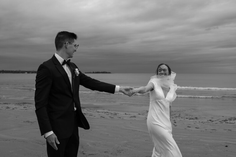 Couple walking hand in hand away from Skogafoss with the wind blowing during their Iceland Elopement