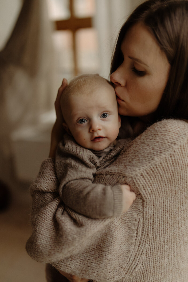 en bebis kollar in i kameran över sin mammas axel