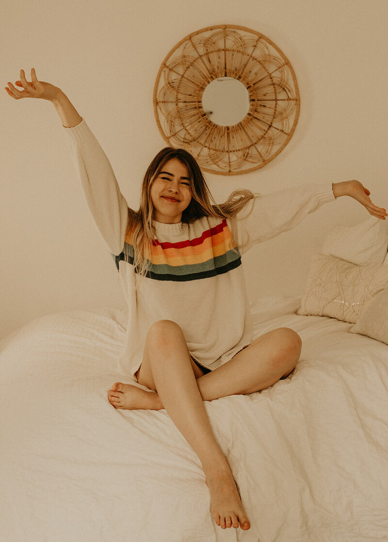 Ciara Corin photo wearing a jacket with a rainbow design sitting on her bed
