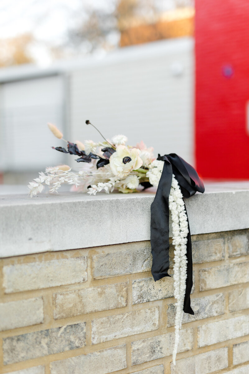 Modern minimalist white and black bouquet wrapped in a black silk cascading ribbon laying on a marble brick wall in Georgetown DC  