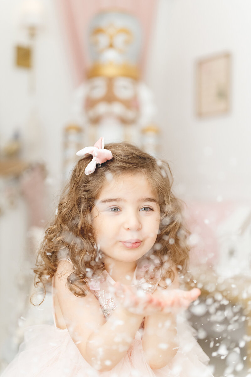 Little girl blowing snowflakes from her hands in a nutcracker themed studio set up for Phoenix holiday mini sessions