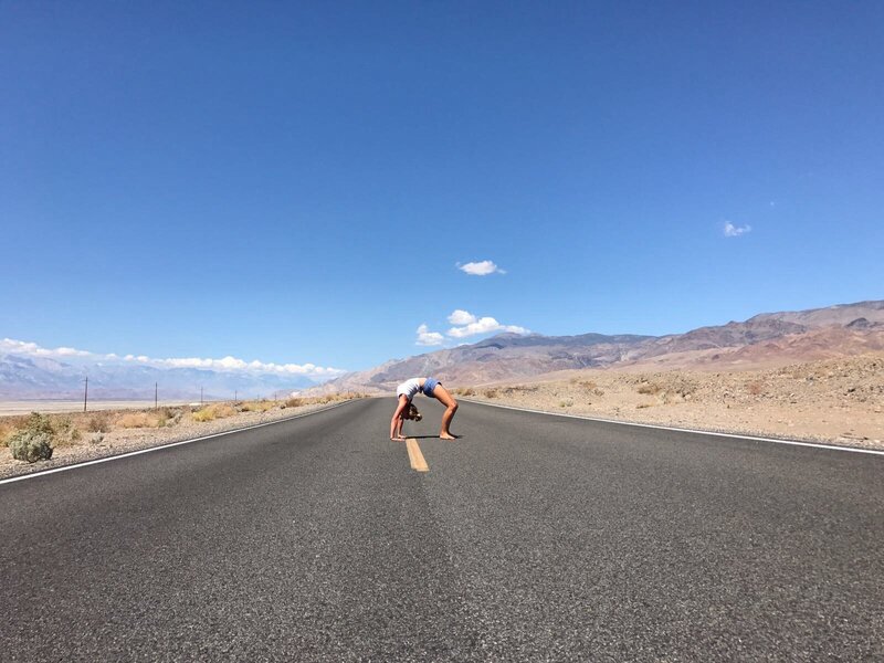Woman doing a yoga pose in the middle of a road surrounded by nature