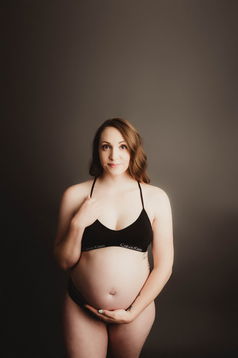 Pregnant mom in black Calvin Klein sports bra  for a studio maternity session.