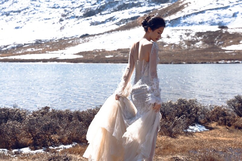Dramatic shoot of a bride in a haute couture dress by an alpine lake in snow capped mountains.