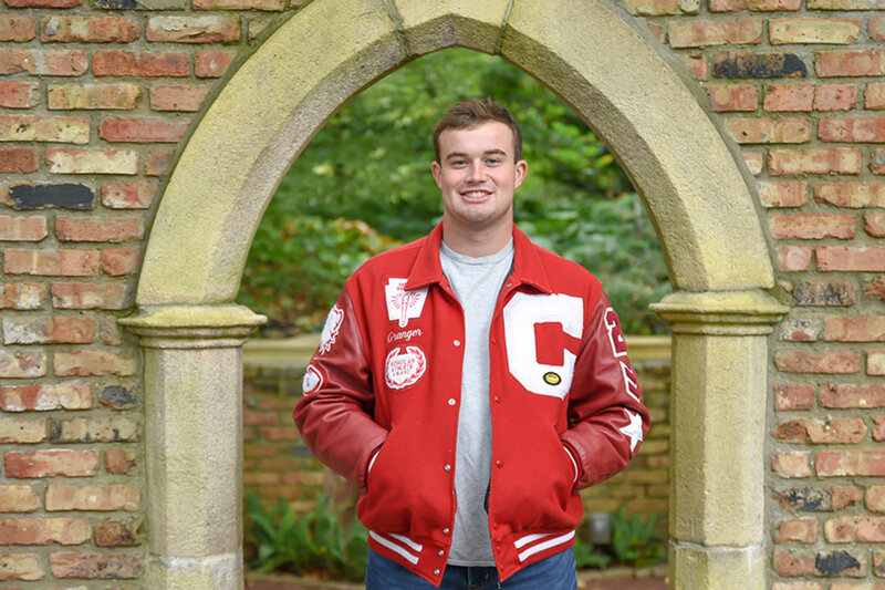 Teenage boy smiles for senior portrait in red letter jacket