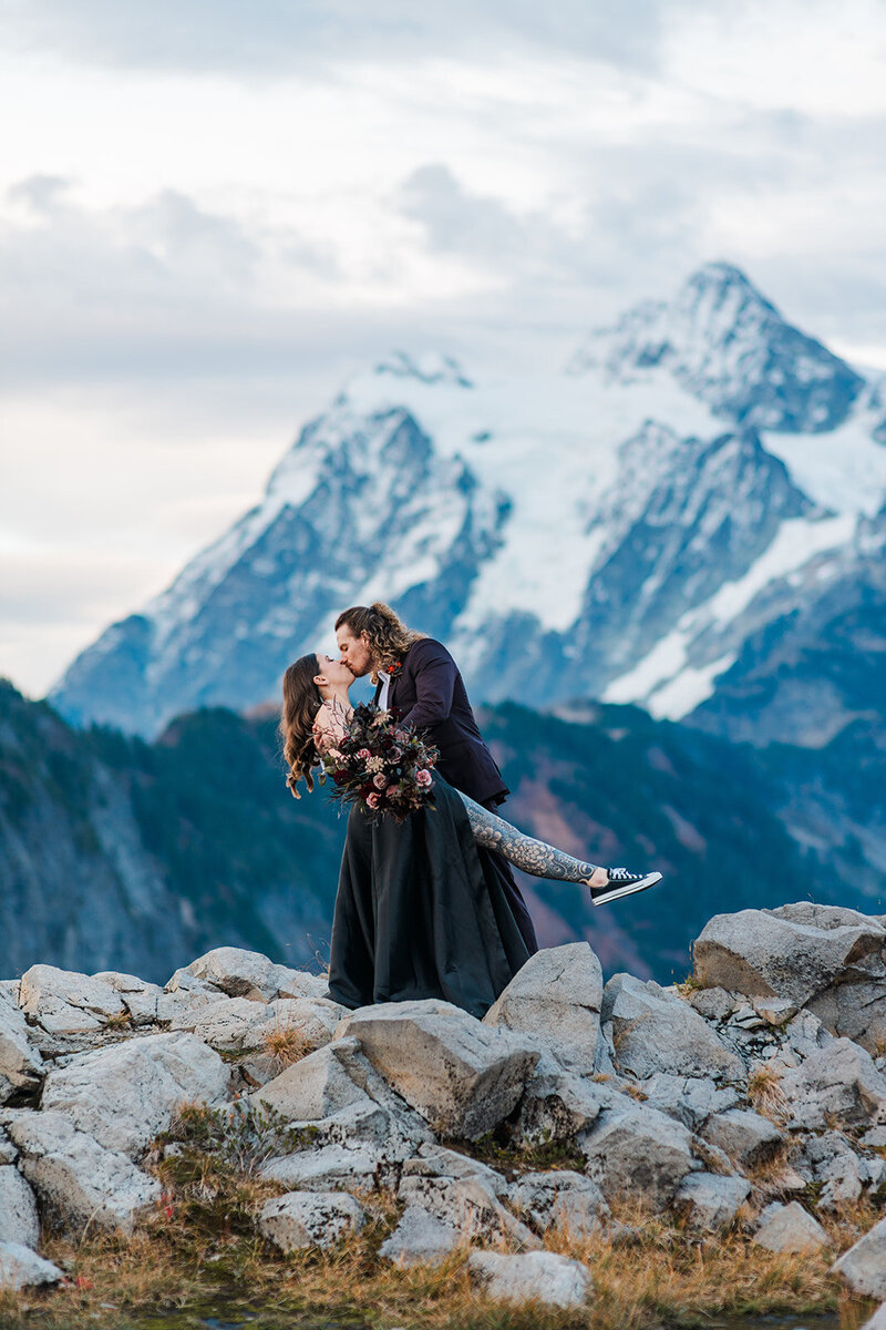 Bride in black dress kissing groom in front of Mount Shuksan during elopement near Mount Baker!