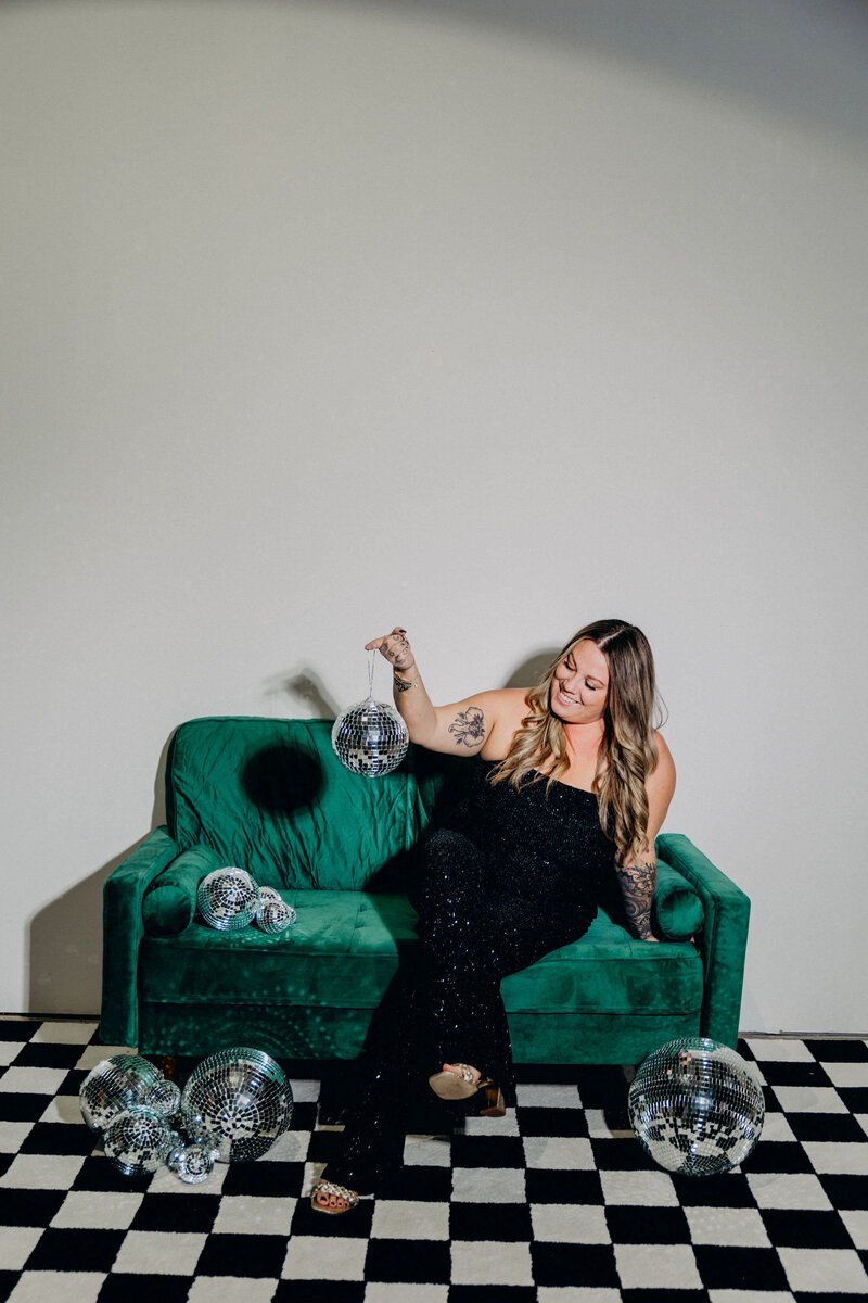 A woman sitting on a green couch in an Austin photo studio with disco balls in her hands.