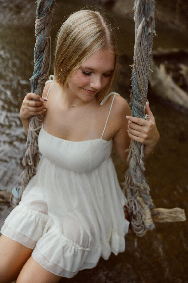 High school senior girl on a rustic swing near the river. 