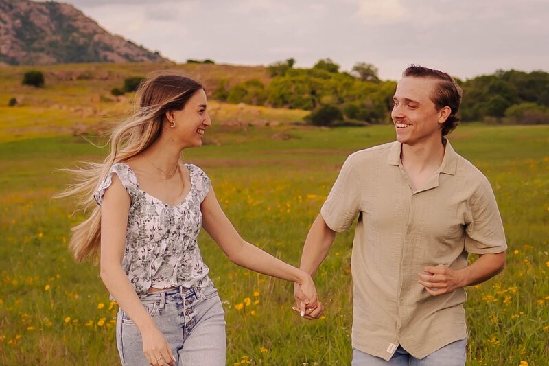 couple running through field holding hands for engagement photos in oklahoma city