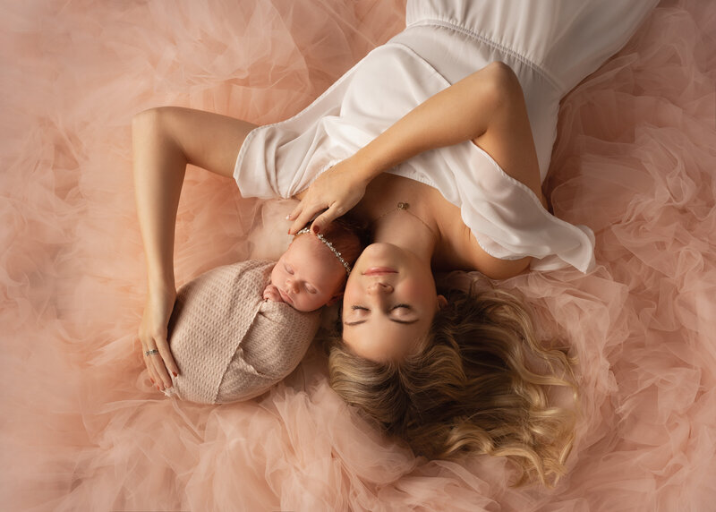 Dreamy mom with baby at newborn photoshoot surrounded by pink tulle and shot from above.