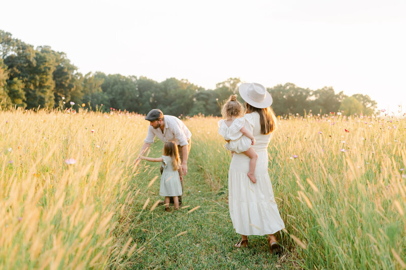 family in neutral clothing plays in wildflower field outside of Philadelphia during a maternity photo session experience.