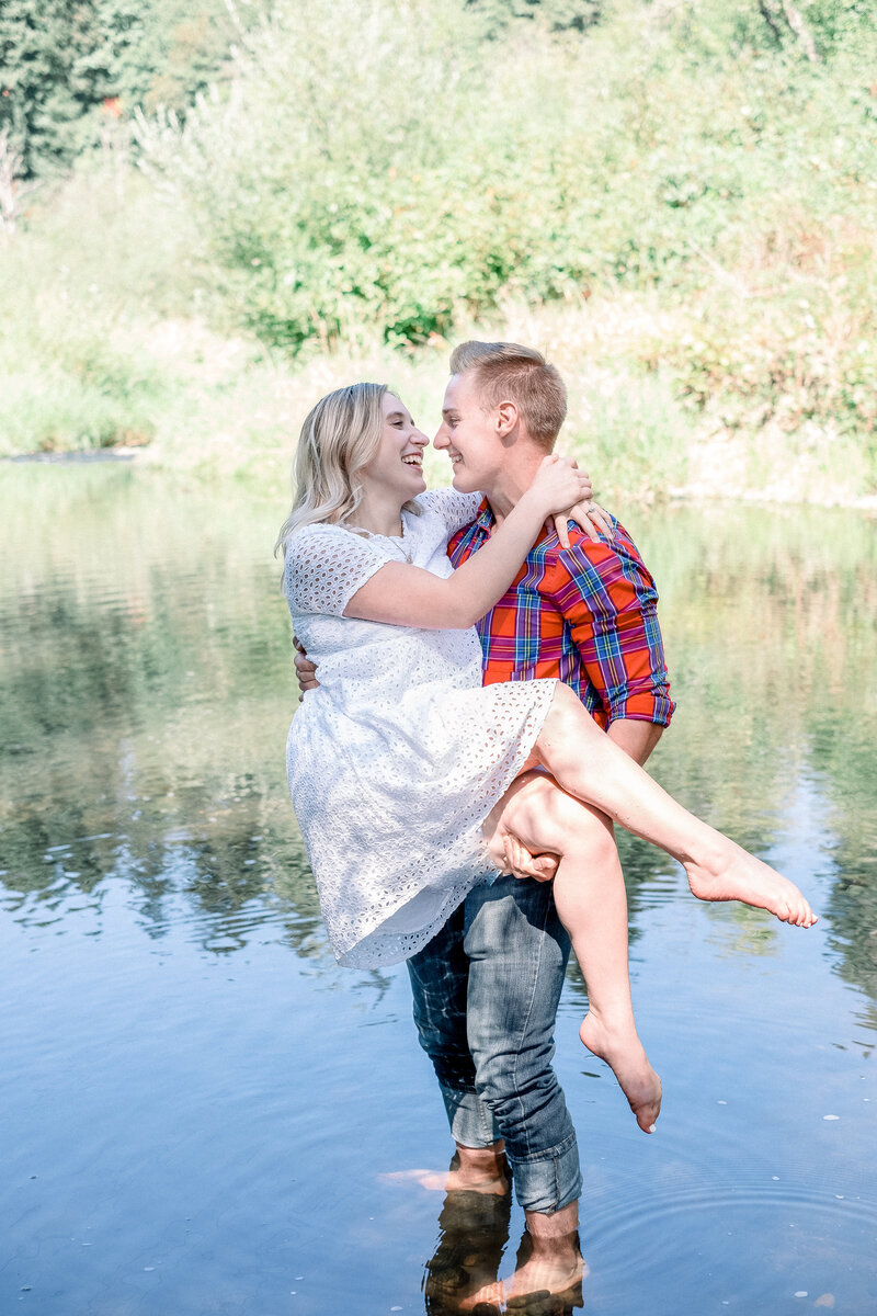 husband holding wife while standing in water both laughing and smiling taken by spokane wedding photographer