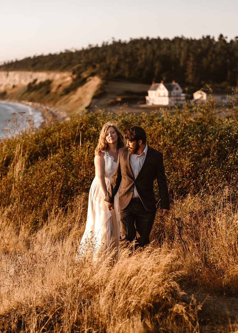 a bride and groom explore a cliffside beach in their wedding attire after eloping in washington state