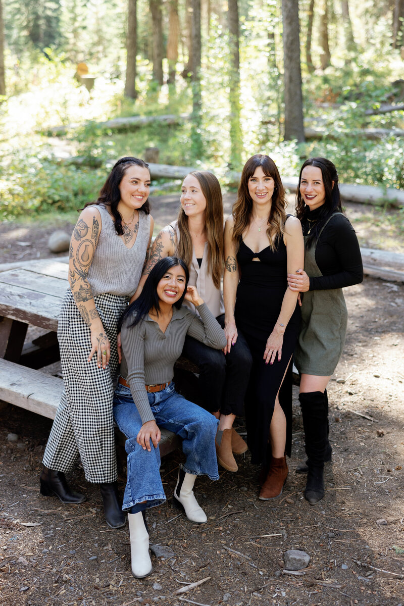 Four women seated on minimalist blocks, striking a confident pose during a team photo shoot that blends style and unity