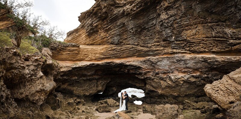 A bride and a groom having a wedding ceremony under the London Bridge rocks in Portsea