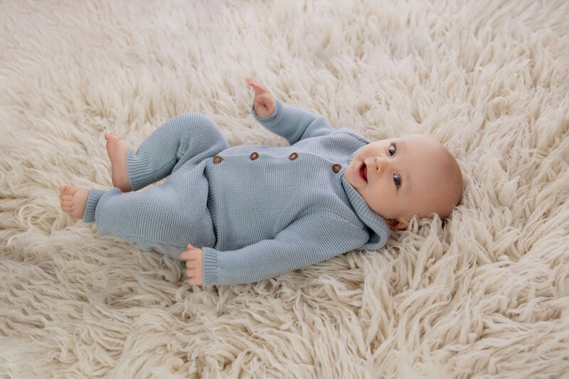 Newborn baby boy in a blue swaddle in a tan basket on a tan background