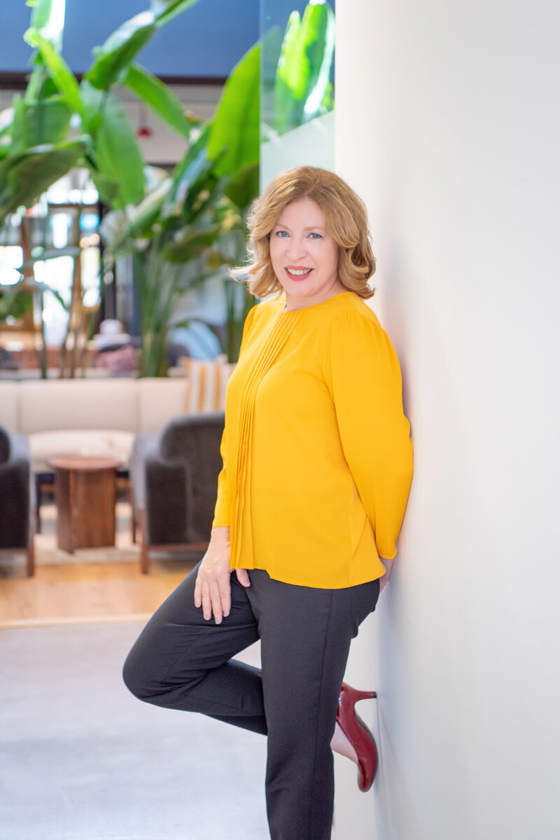 A female social media manager in a yellow top posing for her branding photoshoot.