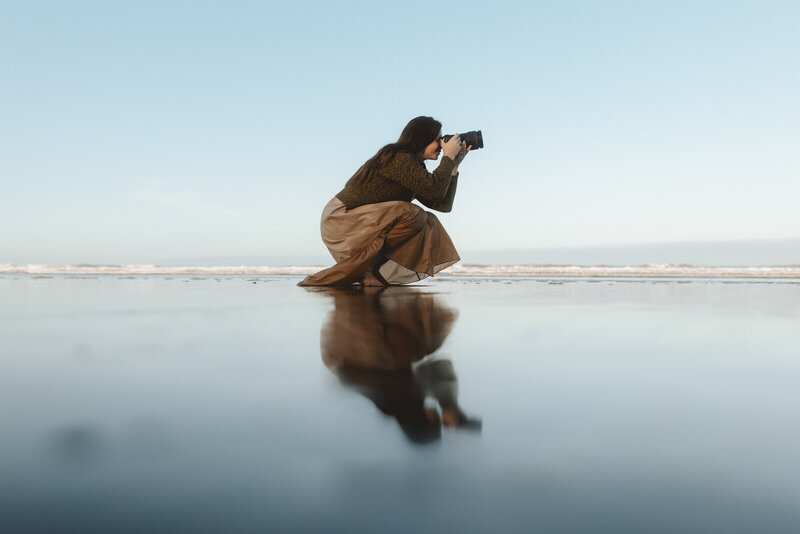 Woman on a pacific northwest beach holding a camera and taking a picture